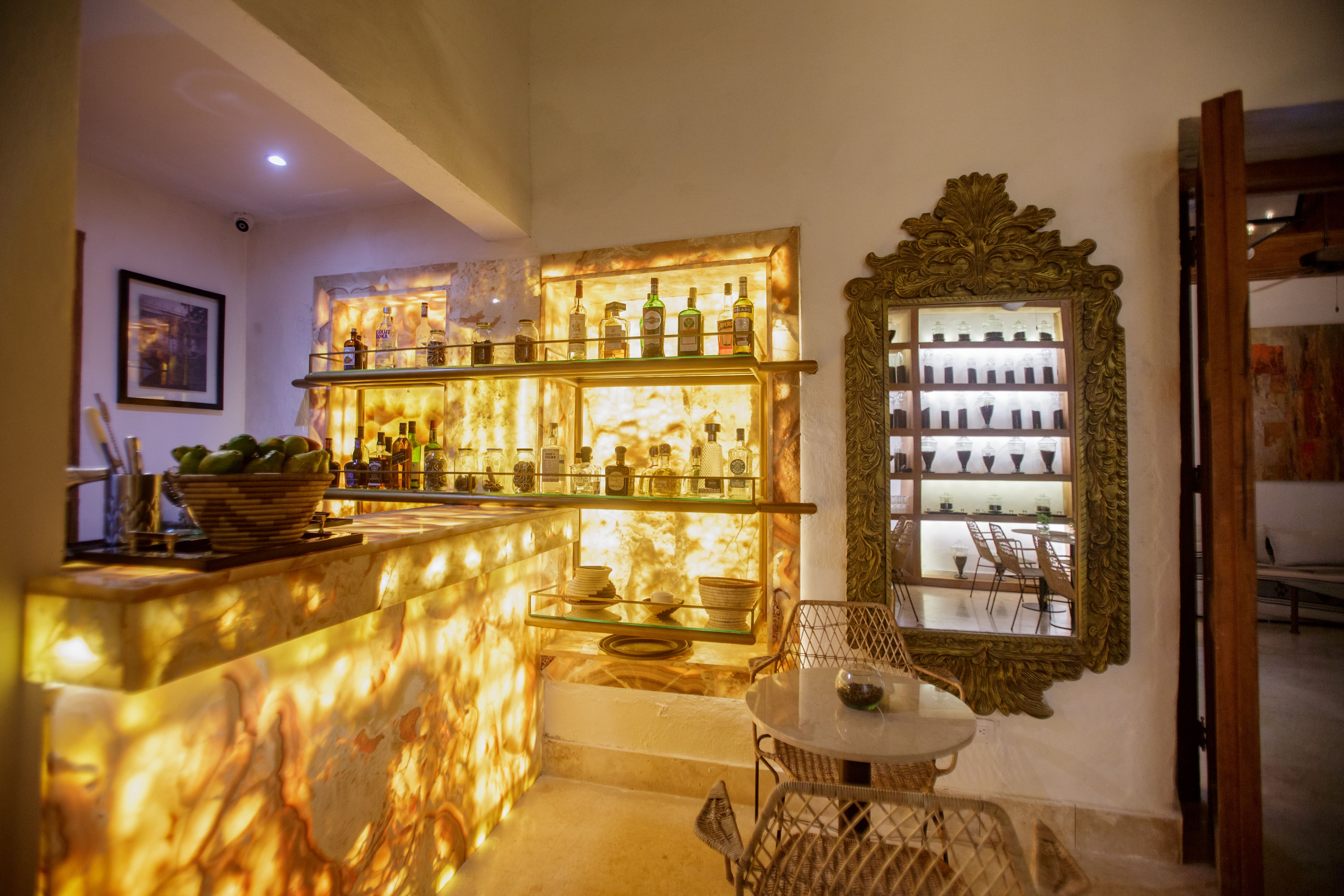 Casa Palmas indoor professional bar with marble counter, premium spirits, crystal glassware, and colonial windows opening to the courtyard